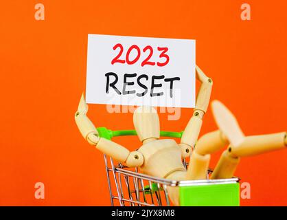 2023 simbolo di ripristino. White paper con parole 2023 Reset, modello umano nel carrello. Bella tavola arancione sfondo arancione. Business e 2023 reset conce Foto Stock