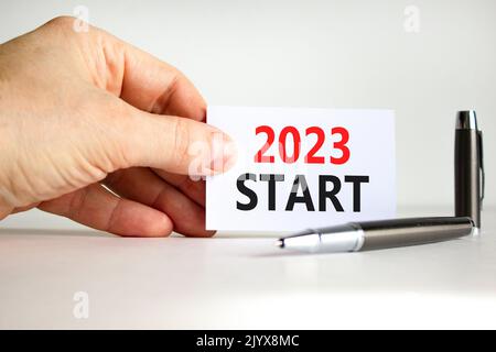 2023 simbolo di avvio. White paper con parole 2023 inizio. Mano uomo d'affari. Penna metallica. Bellissimo sfondo bianco tavolo. Business e inizio 2023 Foto Stock