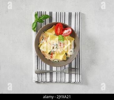 Ravioli tradizionali italiani con ricotta nel piatto con salsa di panna acida con pomodori e spinaci, vista dall'alto Foto Stock