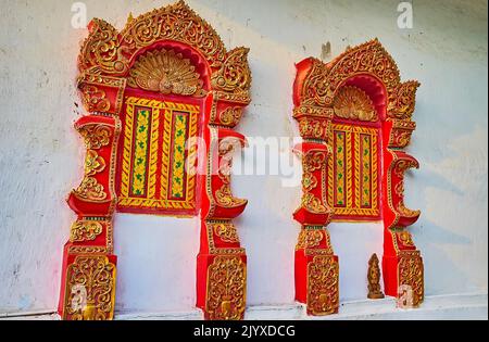 La finestra in rilievo rosso-dorato si apre sulle pareti bianche del santuario dello storico tempio di Wat Pa Kham, Pai, Thailandia Foto Stock