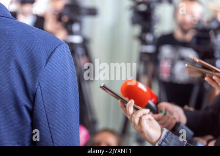 I giornalisti alla conferenza stampa tenendo microfono e smartphone facendo un'intervista mediatica con un politico irriconoscibile o una persona d'affari Foto Stock