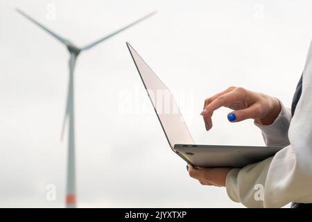 Primo piano donna utilizza un computer portatile per controllare il lavoro del mulino a vento contro il cielo grigio. Foto Stock