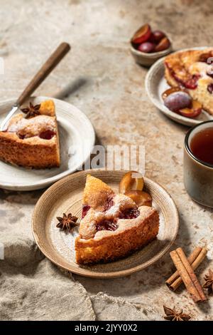 Pezzi della famosa torta di prugna del New York Times o torta con spezie e tè sullo sfondo testurizzato stile rustico. Spazio per il testo. Orientamento verticale Foto Stock