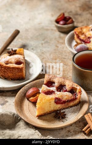 Pezzi della famosa torta di prugna del New York Times o torta con spezie e tè sullo sfondo testurizzato stile rustico. Spazio per il testo. Orientamento verticale Foto Stock