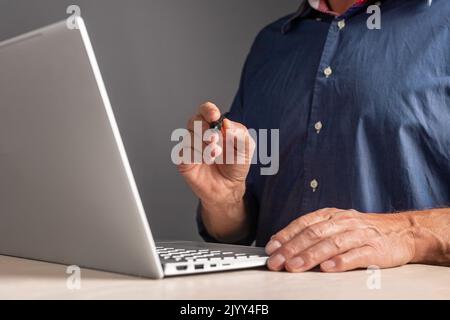 Firma elettronica. Uomo seduto al tavolo con un computer portatile e una penna per firmare un documento elettronico. Tecnologie dell'informazione sul lavoro, ambiente di lavoro senza carta c Foto Stock