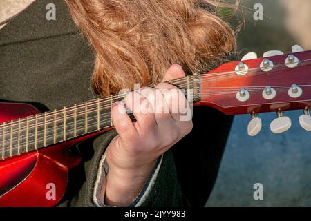 Un giovane gioca il mandolino in città per strada. Mani ravvicinate. Foto Stock