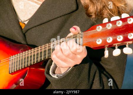 Un giovane gioca il mandolino in città per strada. Mani ravvicinate. Foto Stock