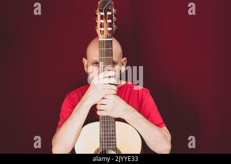 Strumento musicale a corda. Chitarrista maschile carismatico maturo. Ragazzo con barba tiene la chitarra. Uomo bearded in una camicia rossa. Musicista esecutore di musica. Foto Stock