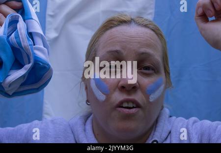 Donna bionda con una bandiera e volto dipinto nei colori dell'Argentina guardando una partita di calcio. Foto Stock