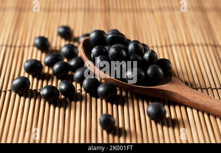 Fagioli di soia neri e cucchiaio di legno posto su sfondo di bambù. Fagioli di soia neri. Foto Stock