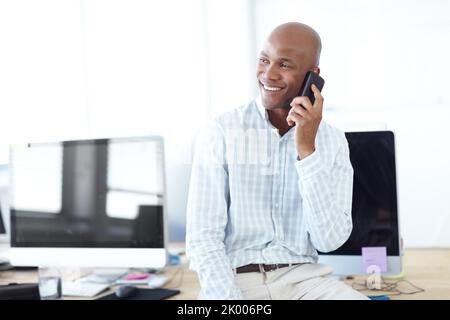 Contattare vecchi colleghi di lavoro. Un giovane uomo d'affari che parla al telefono mentre si siede su una scrivania con computer. Foto Stock