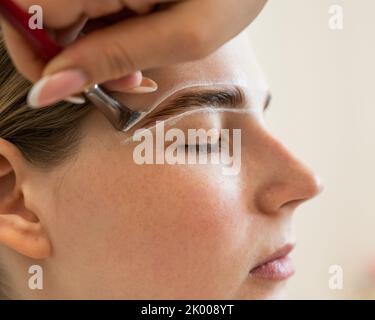 Il maestro disegna la forma delle sopracciglia con vernice bianca prima di colorarle. Foto Stock