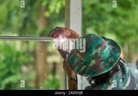 Un saldatore al lavoro all'aperto con uno sfondo verde lussureggiante. Foto Stock