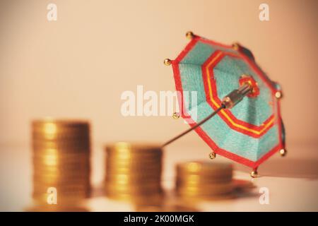 Pila di monete in cima ad un banco di banca con un ombrello . Foto Stock