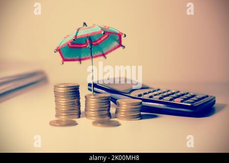 Pila di monete in cima ad un banco di banca con un ombrello . Foto Stock