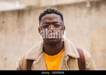 Giovane studente afro-americano che guarda seriamente la macchina fotografica che si alza fuori dalla scuola superiore. Primo piano ritratto di adolescenti intelligente con googles a. Foto Stock