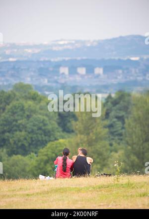 Vista posteriore/posteriore dell'uomo e della donna seduti isolati insieme sulla collina rurale del Regno Unito guardando la vista della città di Birmingham in lontananza. Foto Stock