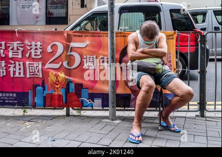 Hong Kong, Cina. 19th ago, 2022. Un uomo dorme in strada accanto a un banner che commemora il 1st luglio della consegna di Hong Kong in Cina a Hong Kong (Foto di Sebastian ng/SOPA Images/Sipa USA) Credit: Sipa USA/Alamy Live News Foto Stock