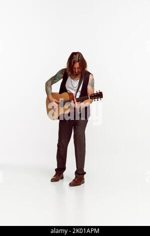 Ritratto di un uomo elegante, musicista rock che suona la chitarra, esecuzione isolata su sfondo bianco studio. Festival Foto Stock