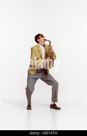 Ritratto di giovane uomo in elegante giacca gialla che suona sassofono isolato su sfondo bianco. Musicista jazz Foto Stock