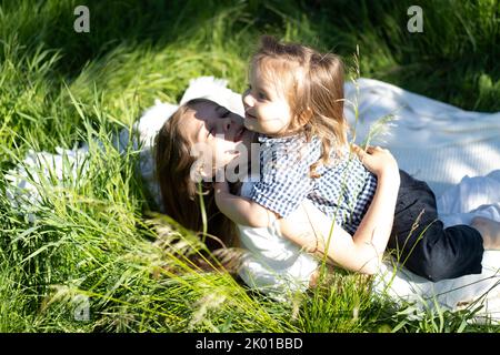 Fratello e sorella abbracciano e ridono felicemente, sdraiati sull'erba verde. Il sole splende, i bambini sono felici spensierati. Il concetto di una vita familiare felice e legame. Spazio di copia. Foto Stock