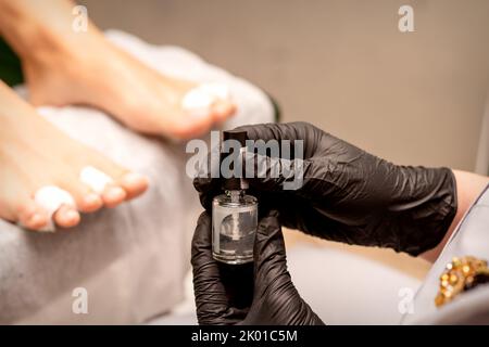 Smalto trasparente per unghie nelle mani di un maestro di manicure mentre dipinge le unghie su un piede femminile Foto Stock