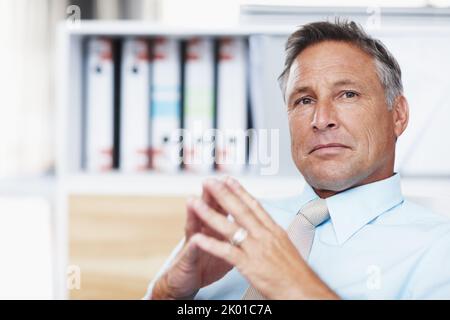 Contemplare la vostra proposta commerciale. Ritratto di un manager aziendale rispettato seduto alla sua scrivania con mani rude. Foto Stock