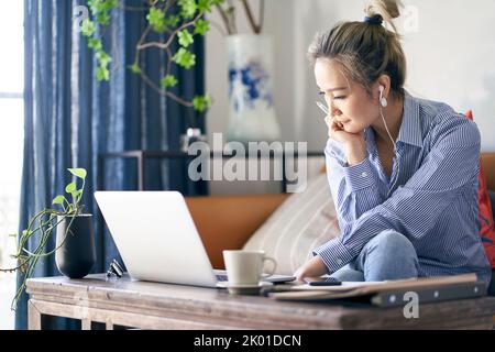 donna asiatica professionista matura che lavora da casa seduto in divano guardando il computer portatile Foto Stock