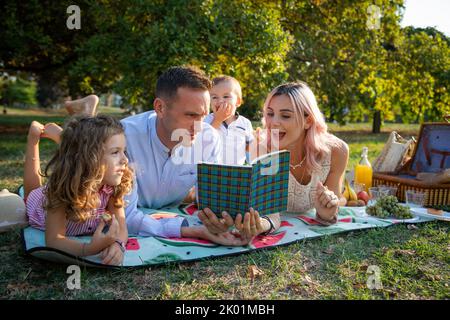 Una famiglia felice in un pic-nic, madre e padre leggere le favole ai bambini Foto Stock