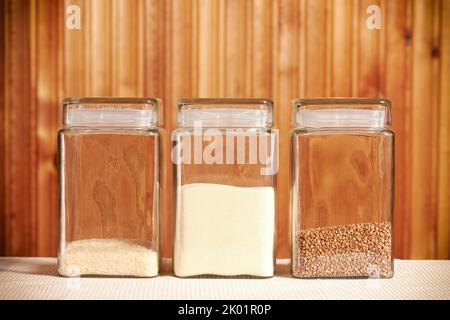 Vasetti trasparenti con semi di riso, grano saraceno e semola. Tavolo da cucina rurale Foto Stock