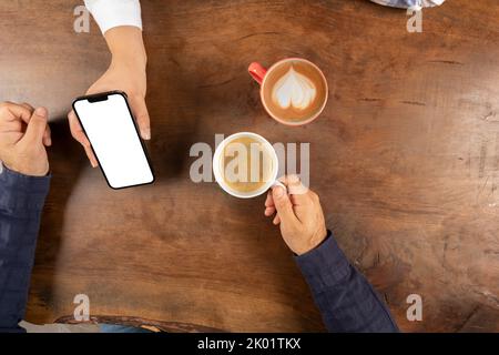 Visualizzazione dello schermo dello smartphone, vista dall'alto di una coppia seduta su un tavolo di legno donna che mostra lo schermo dello smartphone. Parlare su idea di video chat. Foto Stock