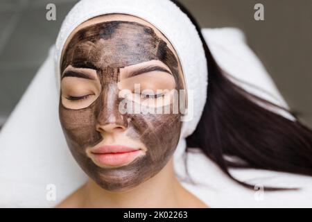 cosmetologo applicazione maschera nera sul viso bella donna indossare guanti neri, donna splendida in spa che hanno le procedure facciali Foto Stock