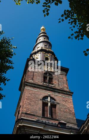 La torre della Chiesa del nostro Salvatore a Copenaghen, in Danimarca, contro il cielo blu d'estate incorniciato da rami d'albero Foto Stock