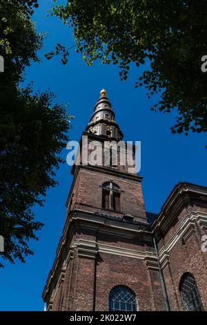 La torre della Chiesa del nostro Salvatore a Copenaghen, in Danimarca, contro il cielo blu d'estate incorniciato da rami d'albero Foto Stock