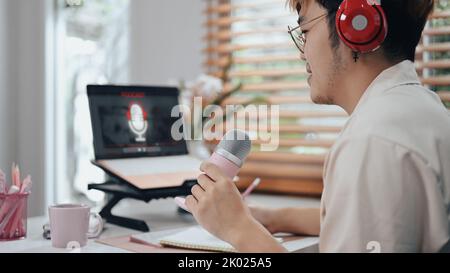 Vista laterale di un maschio che utilizza un portatile e un microfono per registrare podcast da casa studio. Concetto di radio, podcast, blog Foto Stock