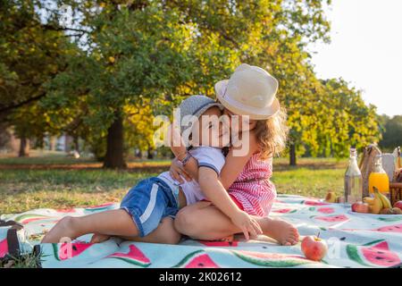 Due fratelli si abbracciano durante un picnic in un parco pubblico, amore per la famiglia Foto Stock