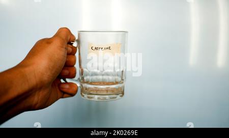 chiudere la mano che tiene il bicchiere vuoto con la parola di testo caffeina scritta sul nastro del condotto Foto Stock