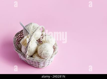 Palle bianche di filo in un cesto su uno sfondo rosa per lavorare a maglia abiti caldi e hobby Foto Stock