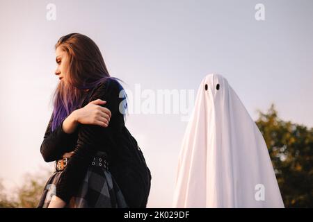 Fantasma in piedi dietro la giovane donna spaventata all'aperto durante Halloween Foto Stock