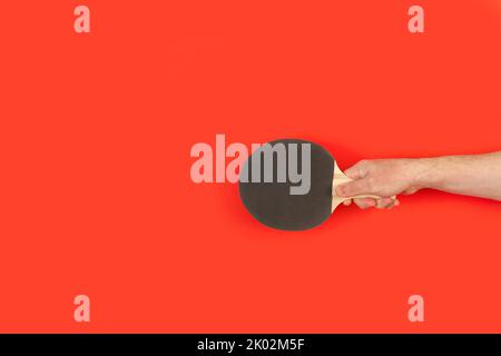 Mano dell'uomo che tiene una pagaia nera del ping pong su uno sfondo rosso Foto Stock