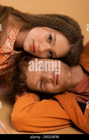 vista dall'alto di un uomo positivo e giovane rosso sdraiato insieme a una bella ragazza isolata su beige, immagine stock Foto Stock