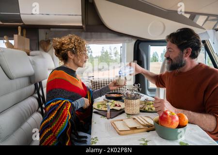 Le coppie adulte possono divertirsi a mangiare all'interno del camper in vacanza in montagna insieme. Uomo e donna in vanlife o attività turistica all'interno del camper. Concetto di casa alternativa di viaggio Foto Stock