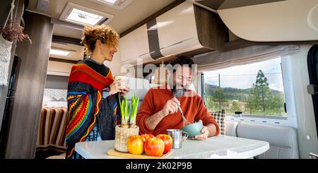 Giovane adulto coppia uomo e donna godere di tempo all'interno di un camper cucina e parlare insieme con amore e amicizia. Concetto di vanlife alternativa e vacanza. Natura boschi all'aperto Foto Stock