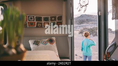 Vista interna di una donna che si erge fuori dal camper e che si diverte da sola per un viaggio all'aperto. Concetto di vita alternativa e di casa. Casa mobile in paese lato immobiliare concetto Foto Stock
