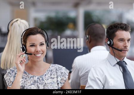 Connessione con i clienti. Un ottimo rappresentante del servizio clienti che prende una chiamata con i colleghi che lavorano in background. Foto Stock