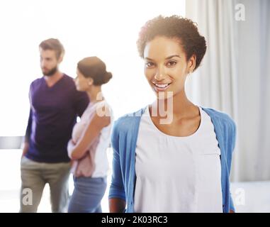 Rappresenta un bene prezioso per questa azienda. Ritratto di una giovane donna d'affari con i suoi colleghi in piedi sullo sfondo. Foto Stock