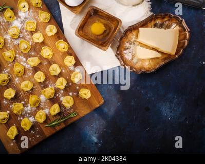 Il processo di produzione di ravioli fatti in casa, gnocchi farciti con carne macinata. Un sacco di ravioli crudi su un tagliere di legno. Ingredienti, cucina utensi Foto Stock