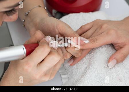 dettaglio in primo piano delle mani di un manicurista chiodi lucidanti in poligel con un tampone elettrico per unghie con punta conica per modellare il chiodo da sotto Foto Stock