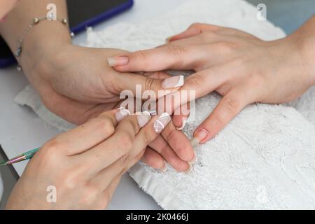 vista dettagliata delle mani di un manicure che esegue una pulizia della cuticola con uno spintore della cuticola. corretta pulizia della mano sinistra di una donna latina. Foto Stock