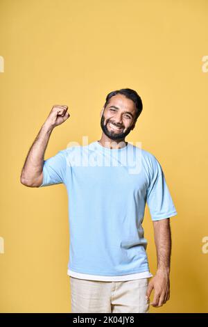 Felice uomo indiano che alza il pugno isolato su sfondo giallo, verticale. Foto Stock